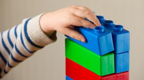 A closeup of a child's hand on some toy bricks stacked up on top of each other. 