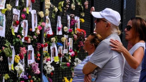 People mourn at the memorial site created by neighbors in front of the partially collapsed building where the rescue personnel continue their search for victims, in Surfside near Miami Beach, Florida, U.S., June 26, 2021.