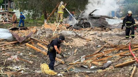 Emergency services clear through the rubble following a Russian missile strike just outside of Kyiv. Firefighters can be seen extinguishing a car fire in the background