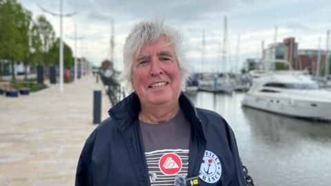 A man standing next to a marina with boats in the background