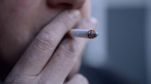 A close up shot of a middle-age man holding a lit cigarette to his mouth. 