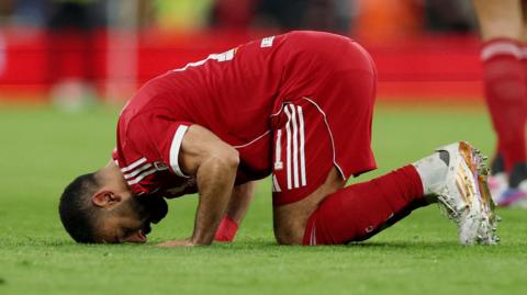 Mohamed Salah kneels on the pitch and touches his head to the ground in prayer after scoring.