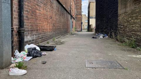 A discarded white shoe and a black bin liner full of rubbish in a side street