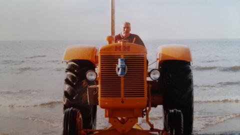 Dave Harrison riding a yellow tractor parked on a beach.