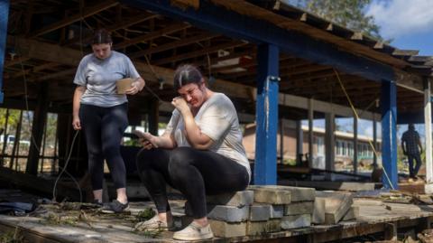 A woman cries as she breaks the news to her sister that the home behind her where they grew up has been gutted by Hurricane Helene, in Horseshoe Beach, Florida