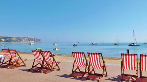 Red and white striped deck chairs lined up in front of the sand at Swanage, Dorset.