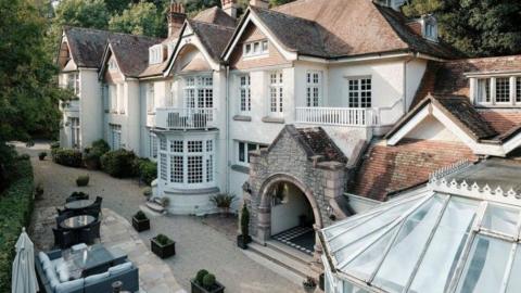 A view of the exterior of Chateau Le Chaire. It is a large white building with many windows. There's a conservatory to the right, and garden furniture to the right.