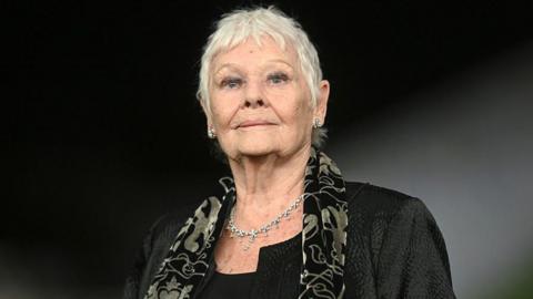 A woman wearing a black suit and a patterned scarf. 