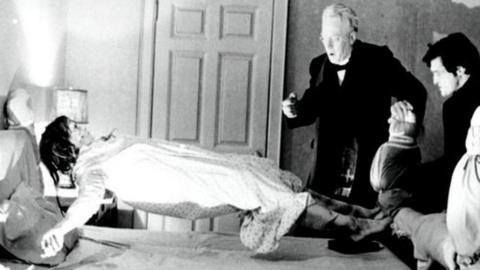 still from The Exorcist in which a girl is levitating as two men watch, looking shocked