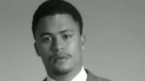 A black‑and‑white portrait photograph of a person wearing a suit jacket, white shirt and tie, facing the camera against a plain background.