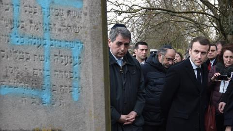 French President Emmanuel Macron looks at a grave vandalised with a swastika during a visit at the Jewish cemetery in Quatzenheim, France, 19 February 2019,