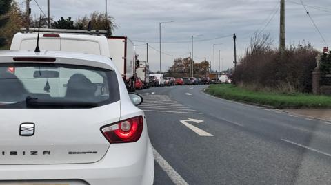A queue of traffic in the left lane extends around a bend. The right lane is clear of oncoming traffic