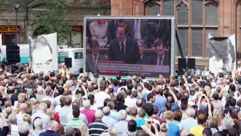 People watch Prime Minister David Cameron on a giant screen making a statement to the House of Commons regarding the findings of the Saville Inquiry into Bloody Sunday, outside the Guildhall in Londonderry.