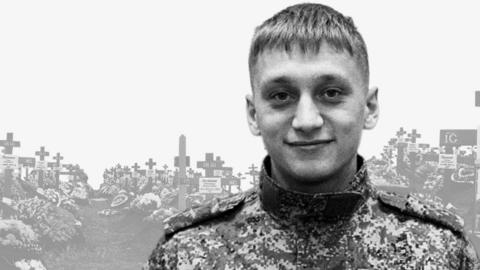Valery Averin in uniform stands in front of an image of a cemetery
