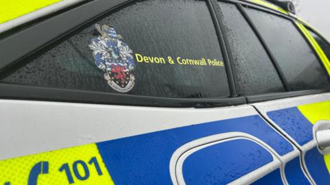 Devon and Cornwall police car zoomed in focusing on the windows, featuring the police badge and the 101 phone number.