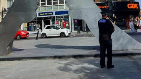 A police officer standing on a high street with their back to the camera 