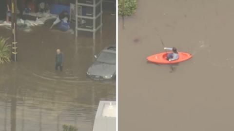 A kayaker is kayaking in a flooded road with another person walking in the road.