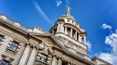 A statue of Lady Justice on top of Old Bailey in London. The building is made of white stone. 