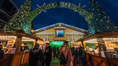 One of the bars at Leeds Christmas Market in 2023, shown at night with Christmas trees and fairy lights 