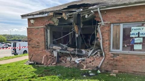 A one-storey brick building with a large hole knocked in one wall and red and white tape to the left