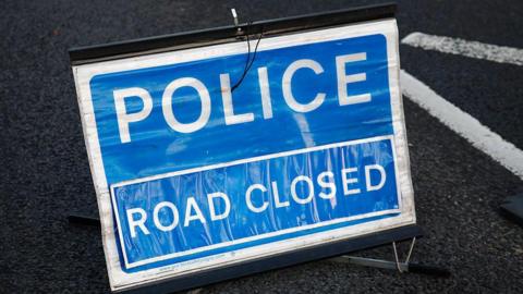 A blue and white sign which reads police, road closed.