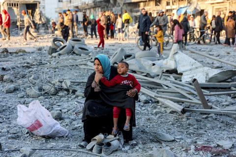 A woman sits with a child with salvaged footwear amidst debris and rubble at the site of Israeli bombardment on a residential block in Gaza City.