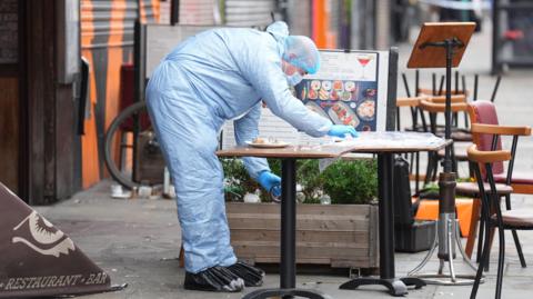 A police forensic officer at the scene of a shooting at Kingsland High Street looking at a table outside a restaurant. 