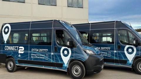 Two minibuses parked side by side, covered in blue branding for the Connect2 service.