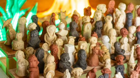 A close-up of about 100 of the clay figures arranged on shelving. They are different colours including white, red and dark brown