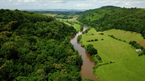 Aerial view of River Wye, with fields and hill on right bank and a forest on the left