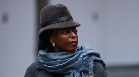 Headshot of Diezani Alison-Madueke looking off-camera wearing a grey brimmed hat with a blue scarf and grey coat.
