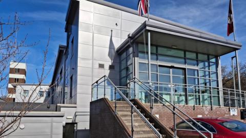 An exterior of a fire authority building, with steel walls and two union jack flags flying outside. There are steps leading to the entrance of the building.