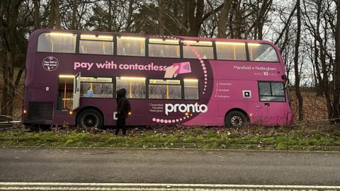 A pink double-decker bus hit a with a tree on the A60 Mansfield Road, near Papplewick, Nottinghamshire. Pictured is the bus on grass next to the road
