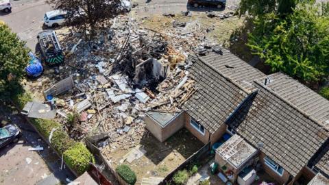 An aerial drone shot of three bungalows, one of which is totally destroyed with