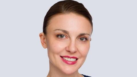 A woman smiles towards the camera, she is wearing red lipstick and has her hair up