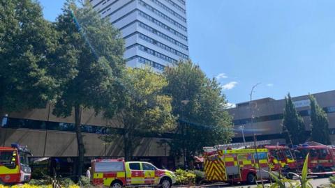 A number of fire engines and emergency vehicles parked in the road outside a tall block of flats.