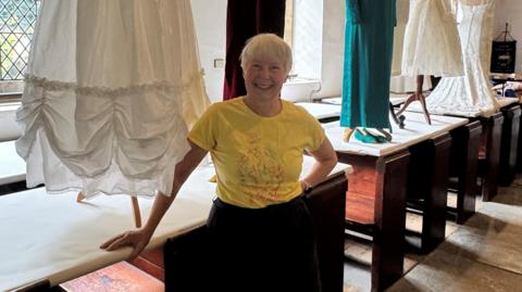 A woman in a yellow T-Shirt and with short hair is standing next to a white skirt which is displayed in a church.