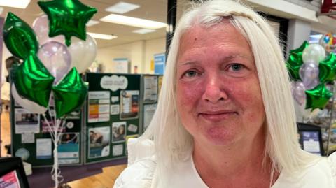Tracy stands outside an empty shop in a shopping centre full of information on social pescribing 

