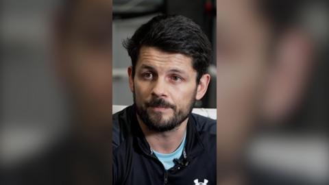 Retired boxer Stephen Smith wears a blue top under a black sport pullover and looks slightly to his right.