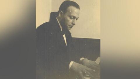 A black and white photo of musician Stephen de Bastion at a piano