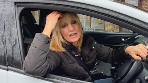 Blonde woman sat in car in driver's seat