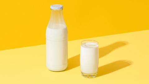 A bottle of milk and a glass of milk on a yellow background