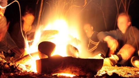 Several people sit around a campfire at night.