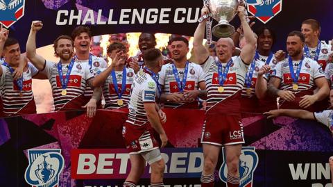 Wigan Warriors players lift the Challenge Cup trophy