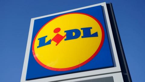 A large Lidl supermarket sign stands under a clear blue sky.