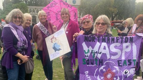 Members of the Northamptonshire Waspi group attend a protest in Westminster in London during the autumn Budget speech. Six women are standing together as they hold purple signs that say "Northampton Waspi  South East"