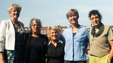 Five women standing with their arms around each other against a blue sky. The women who founded the first Women's Rugby World Cup in Cardiff, 1991.