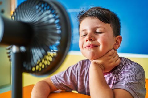 A boy stands in front of a fan in a classroom