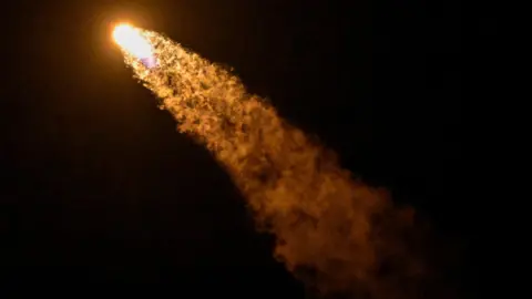 A SpaceX Falcon 9 rocket and Dragon spacecraft leaves an orange trail as it blasts off into space