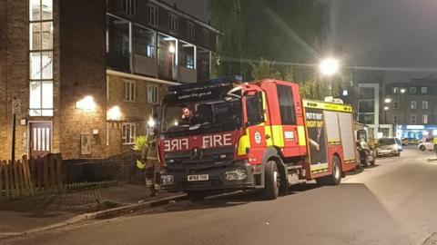 A fire engine parks next to a maisonette in the dark